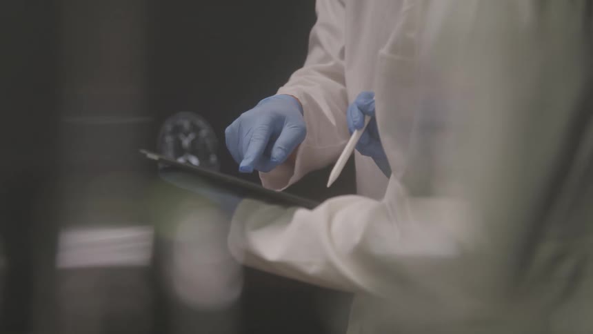 Two people wearing gloves holding pens and interacting with a device in a lab