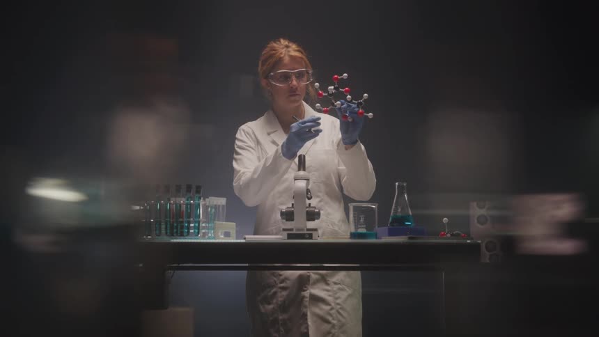 Female scientist studies molecular model in dim lab