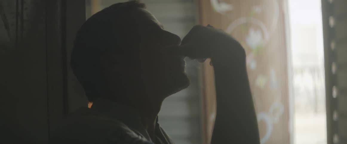 A man is sitting in a dark room touching his face