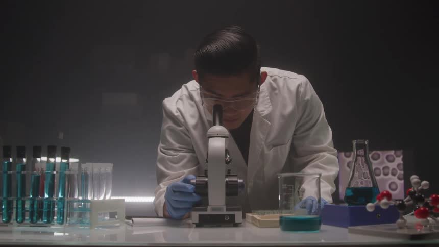 Young asian male scientist looks into a microscope lens to observe a slide in a lab