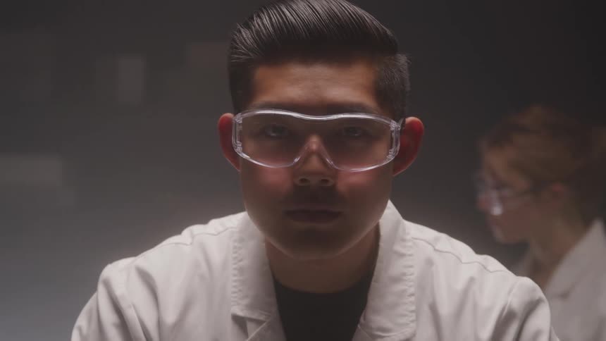 Man in white coat with glasses in an indoor laboratory setting