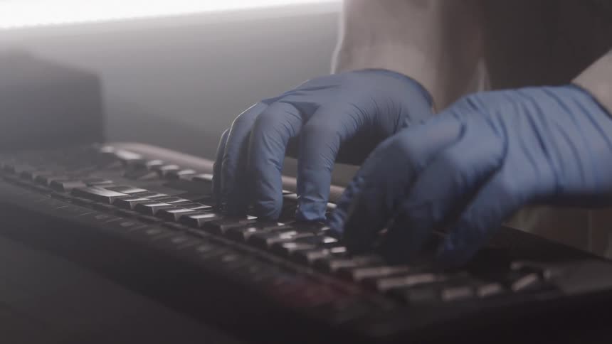 Close up of a gloved scientist typing with a computer keyboard in a lab