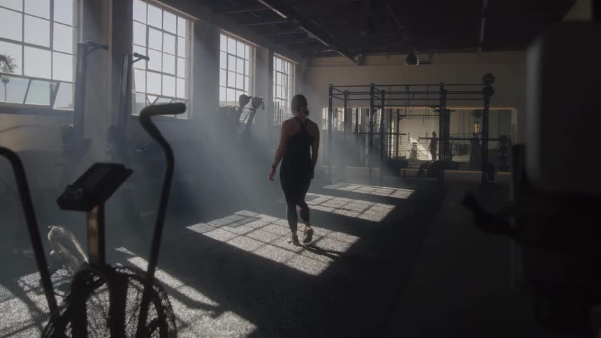 A young woman walks away towards a gym equipment in the gym during daytime