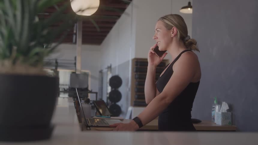 A woman at a gym reception desk is on the phone call