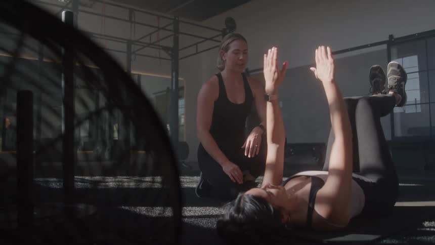 Trainer coaches woman doing leg raise exercises in a gym