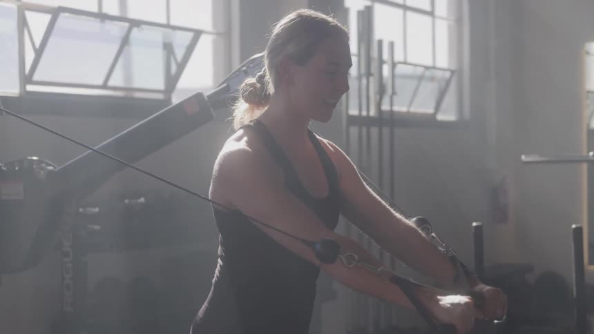 A young woman performs cable pulls in the gym during daytime
