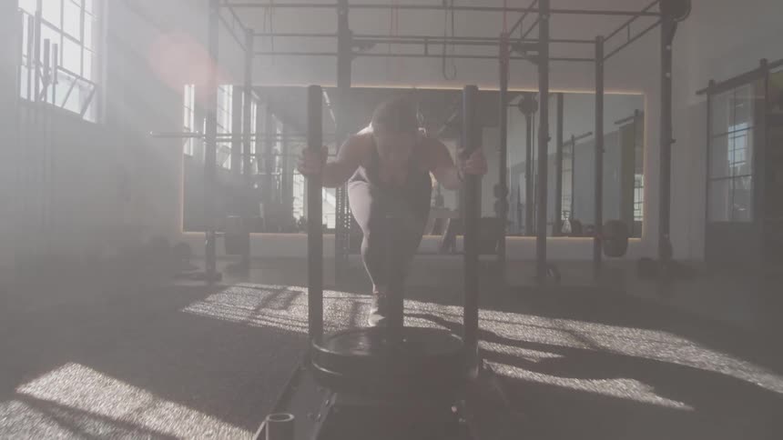 Woman pushing a machine with weight plates at a crossfit gym