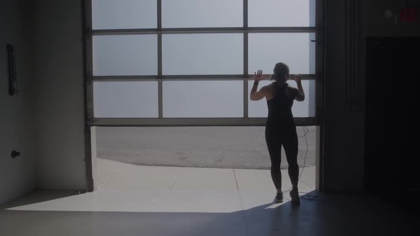 A woman in an exercise outfit opens the door to a large empty garage
