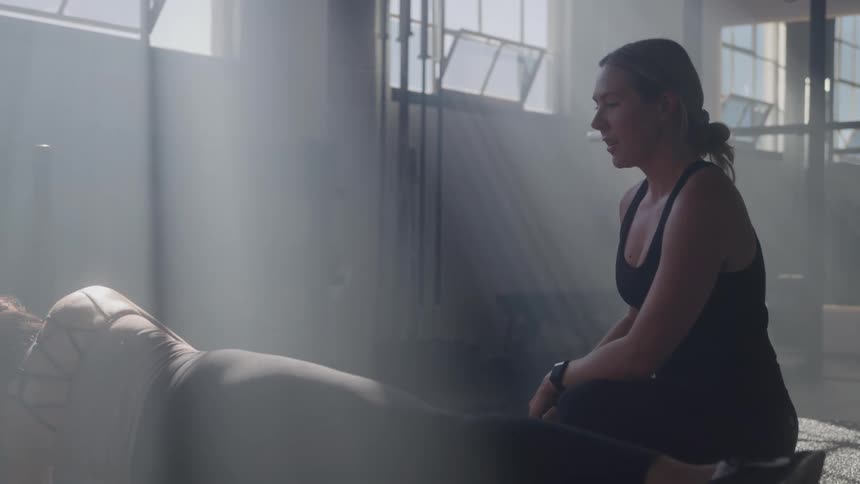 Personal trainer helps her client perform stretching and strength exercises at the gym