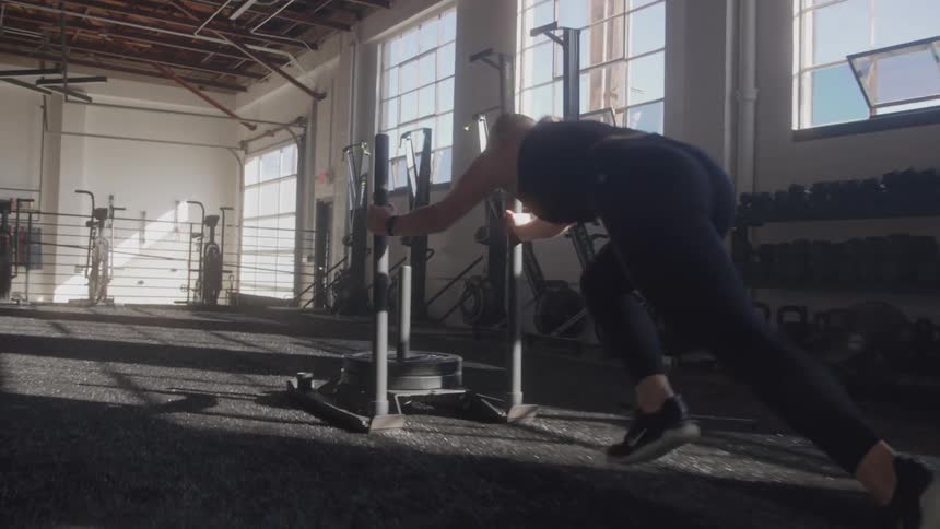 Woman doing weighted sled push exercise in a gym