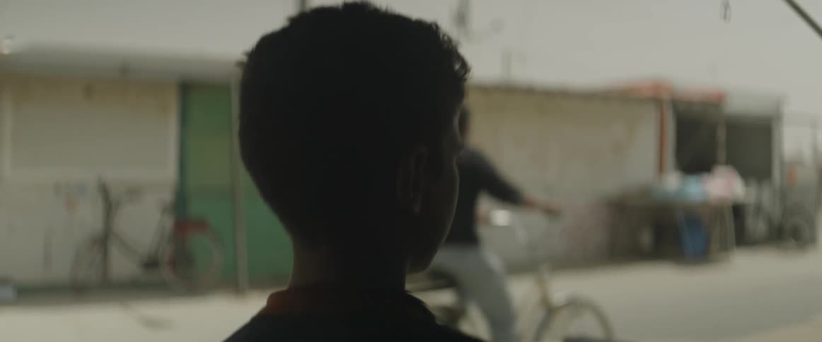 A boy looks out towards a street as a bicyclist rides by