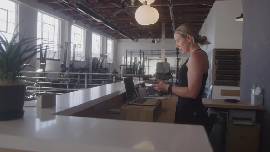 The woman is writing and using a laptop in the gym