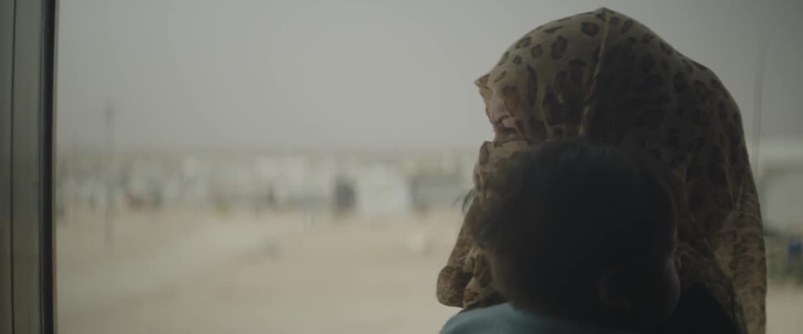 A woman holding a baby looks out across a desert