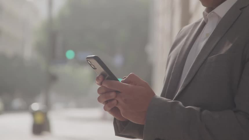 A businessman uses a smartphone on a city street