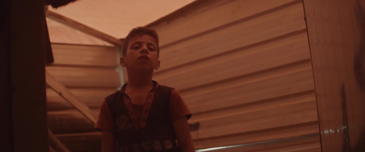 A young boy stands near a wall