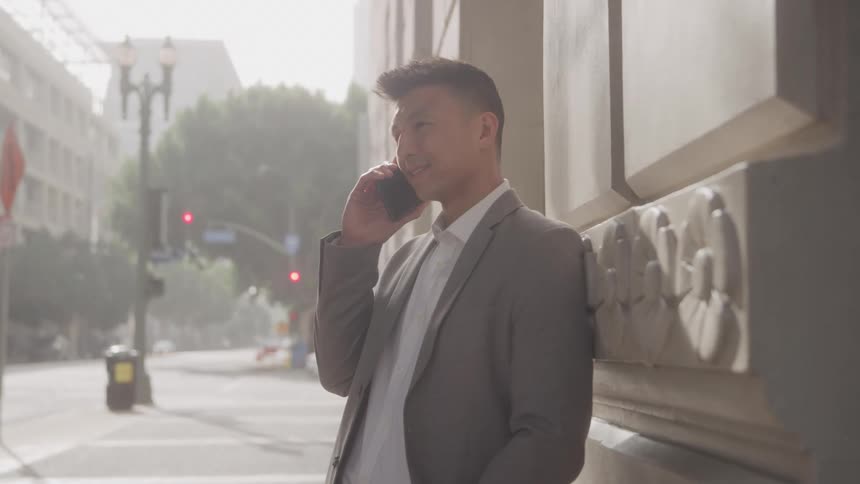 The man is leaning against the building using his cell phone
