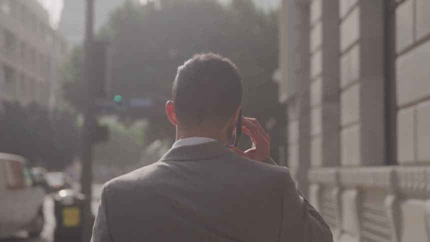 Person in a suit walking on a sidewalk talking on a call on a smartphone