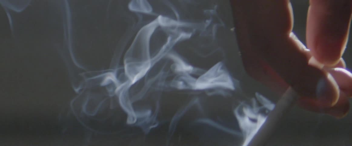 A hand is dangling with a lit cigarette