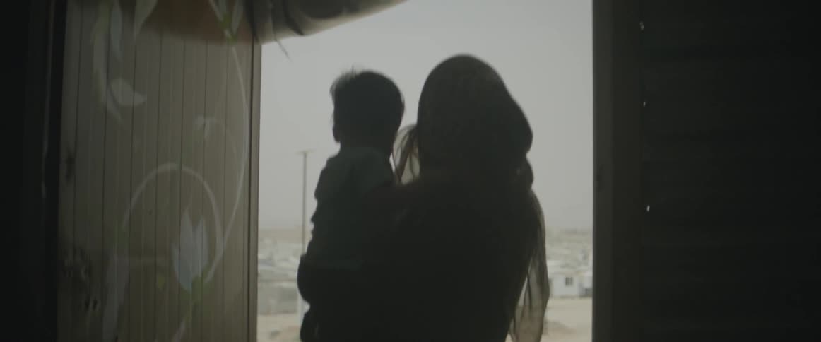 A woman wearing a headscarf holds a baby and looks outside