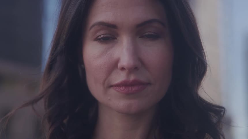 A woman with long brown hair and red lipstick is outdoors