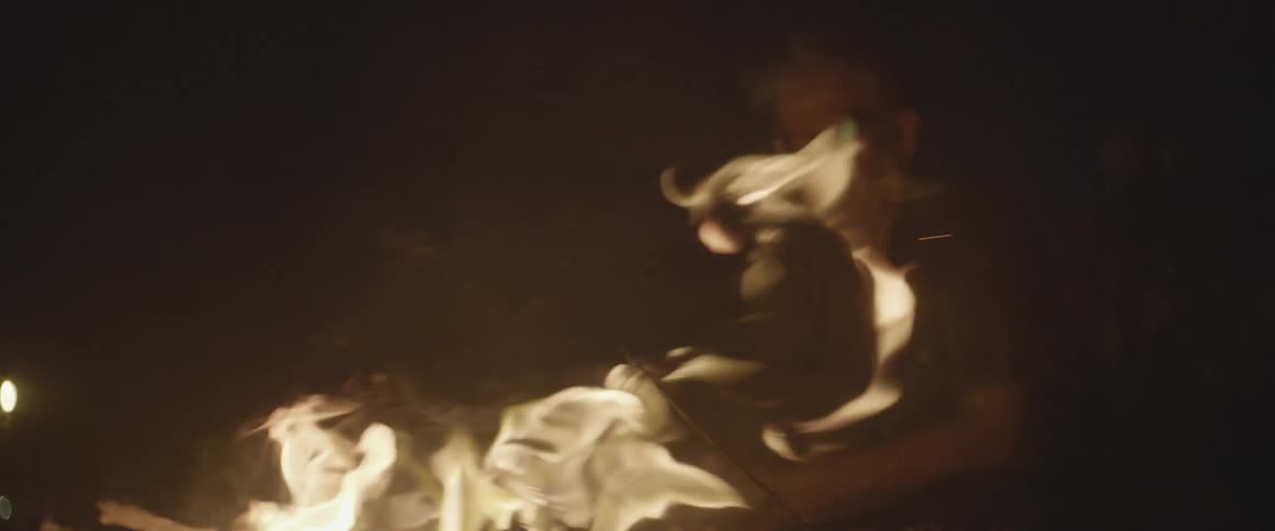 A man stands by a large campfire at night