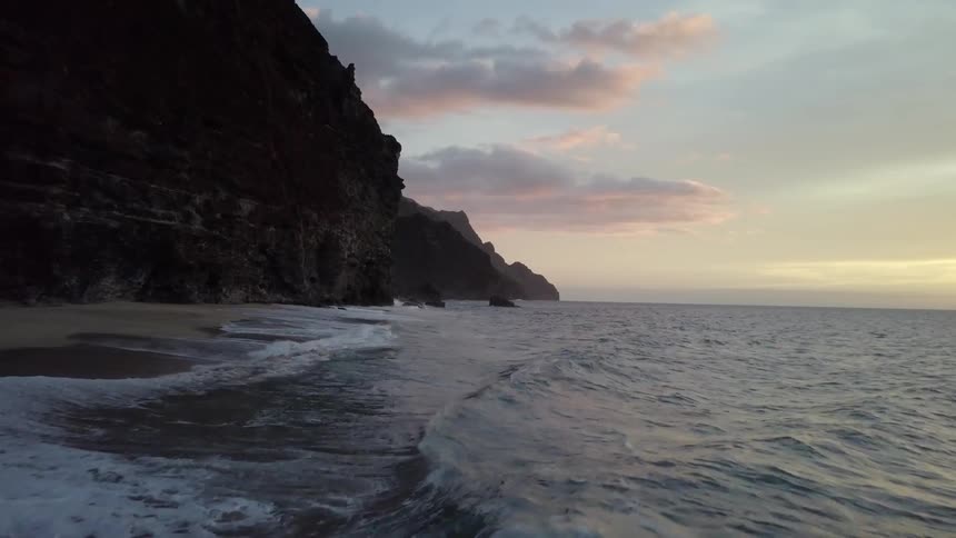 Waves roll onto a shore near a large, rocky hill