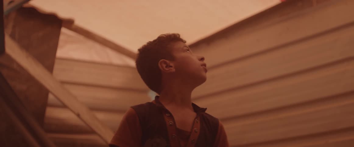 A boy looking up and the roof of some building that looks like a wooden tent