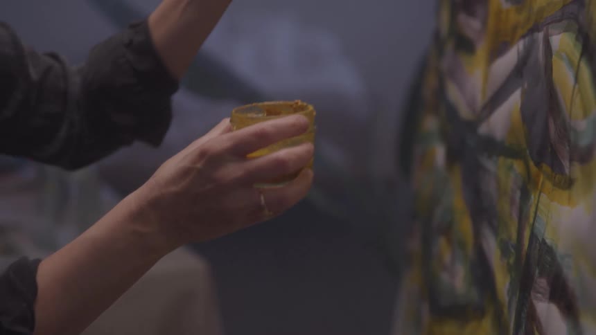 Person holding a paintbrush and a cup of paint painting a canvas