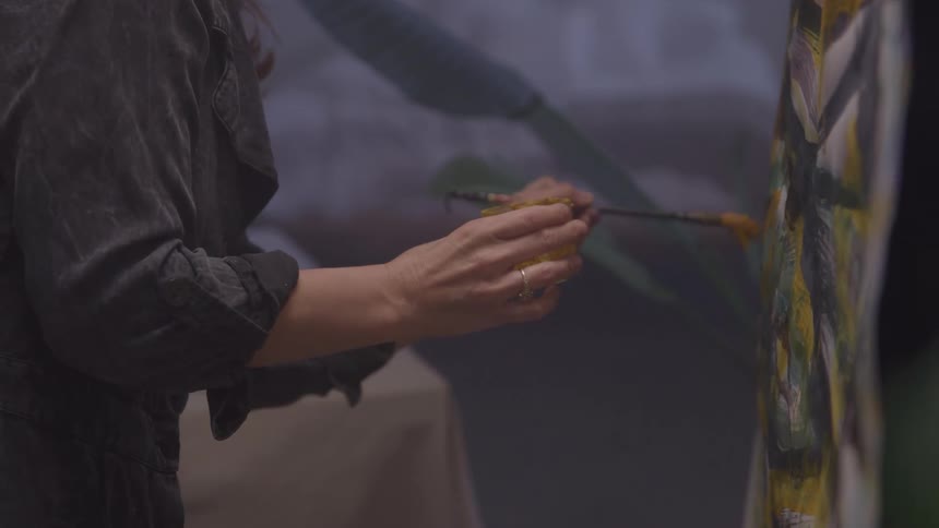 An artist paints on a canvas indoors