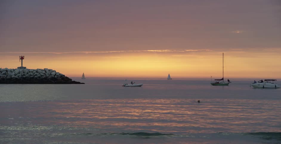 Boats move on ocean near lighthouse at sunset