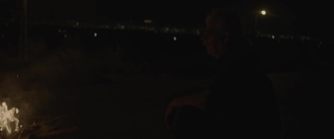 A man sits by an outdoor fire