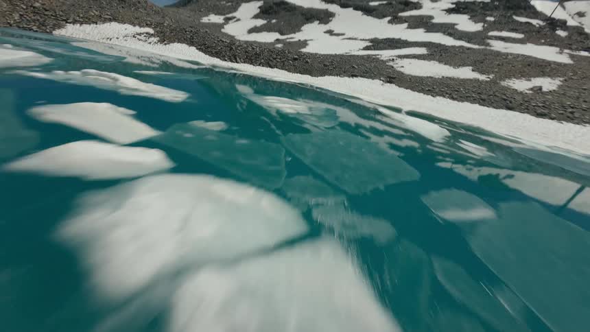 A partially frozen lake with cracked ice patterns lies at the edge of a snowy shoreline