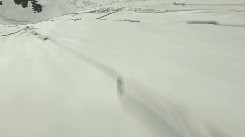 A vast stretch of snow blankets a rugged mountain slope its textured surface etched with natural creases and lines as it flows downward