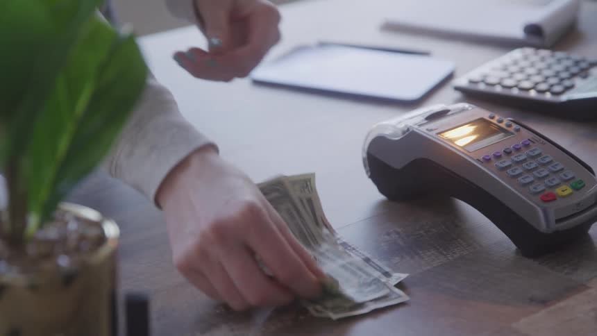 Person counting dollar bills next to a card machine