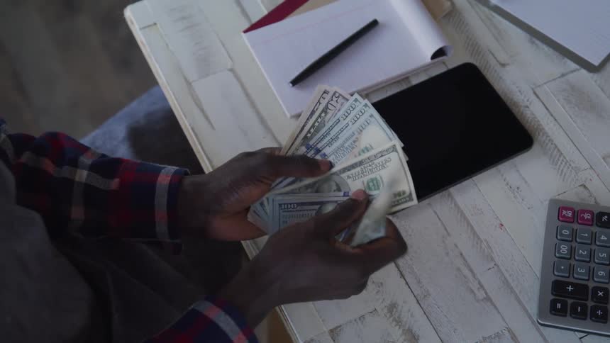 The man sits by the desk counting money