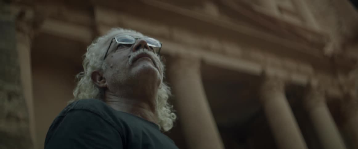 An older man is looking up at ancient ruins