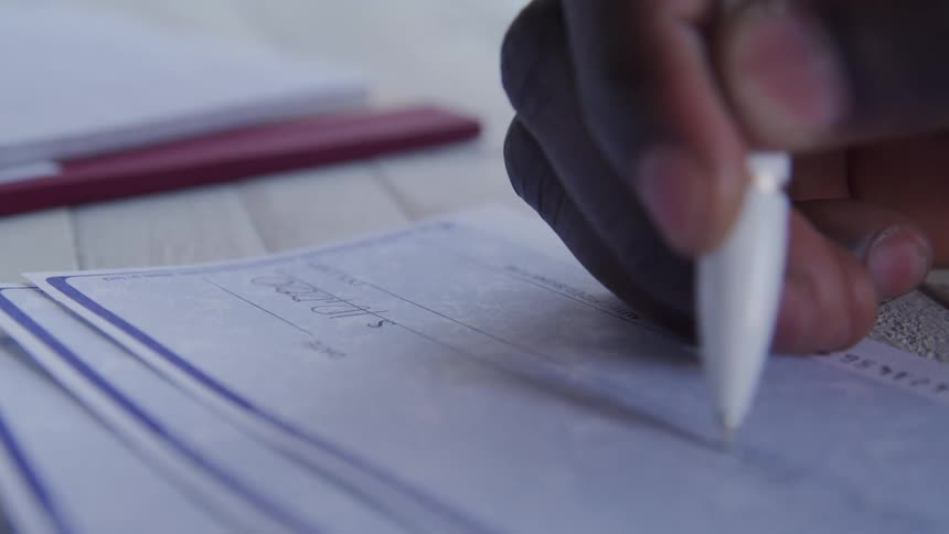 A person filling in an amount and signing a bank check