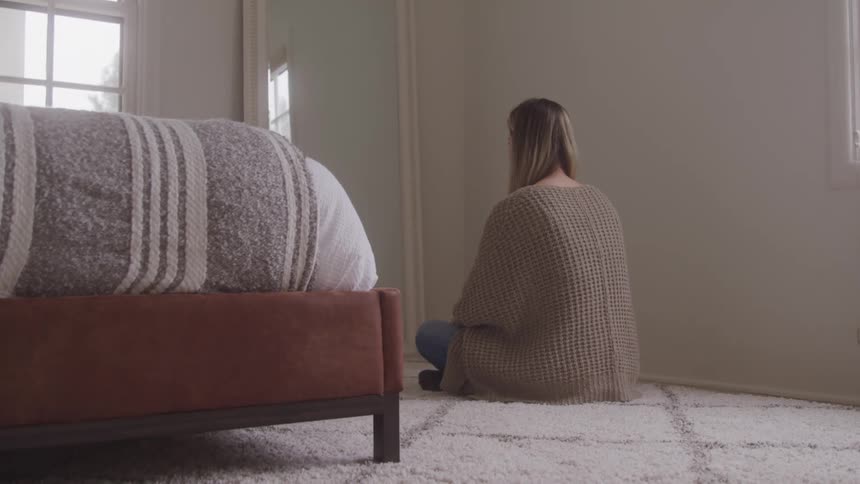 A woman is sitting on the carpet in the bedroom