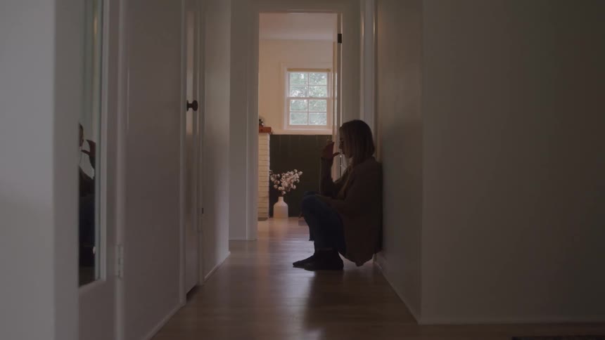 A woman standing against the wall slowly sits down dramatically and breaks down in tears and sadness