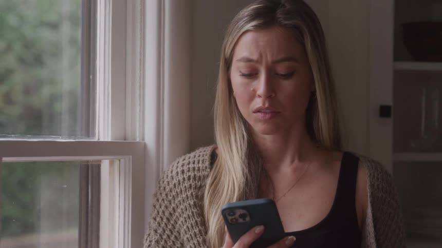 A woman sadly looks at her phone