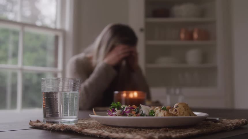 A woman sadly sits at the kitchen table