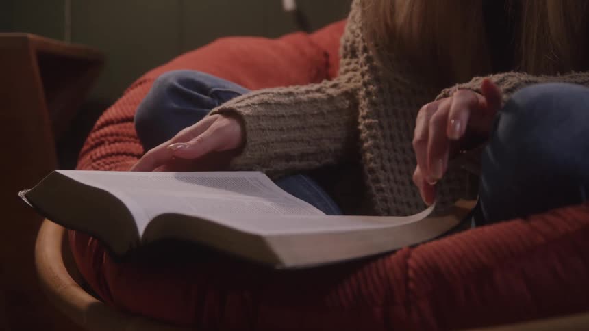 Person seated in an armchair flips through an open book with small print