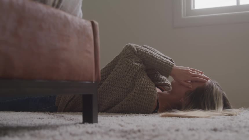 The woman laying on the carpet puts her hands on her face