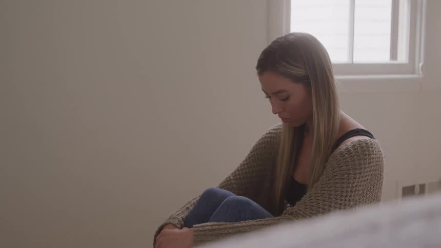 Woman sitting with hands on knee with sad expression