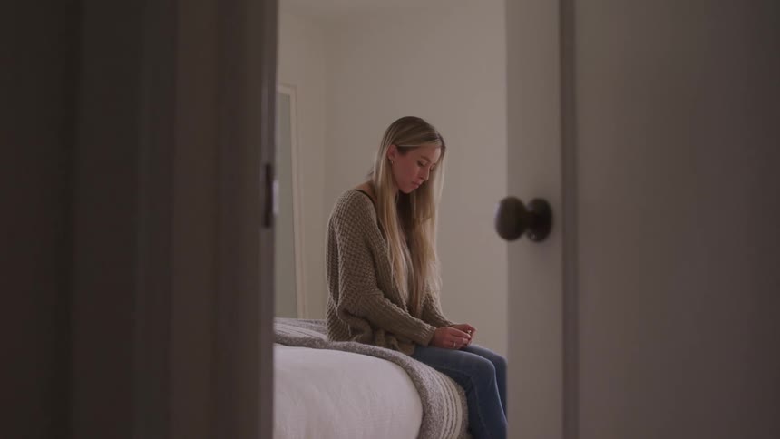 A woman sadly sits on a bed