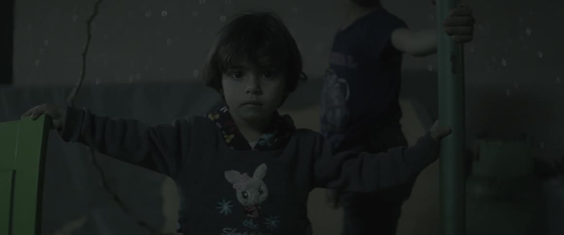 Children stand gripping a metal pole in a dark environment