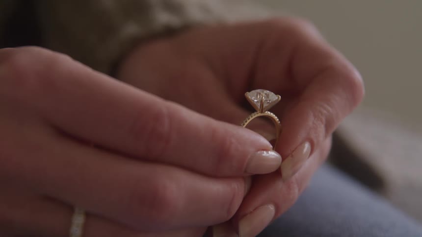 A woman holds an engagement ring between her fingers