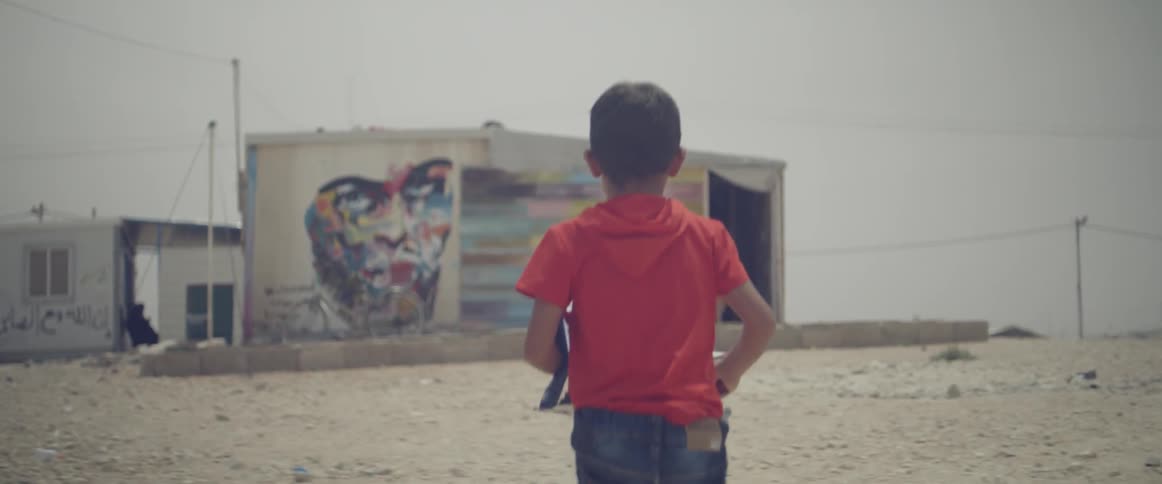 A young boy runs outside near a building with a wall mural