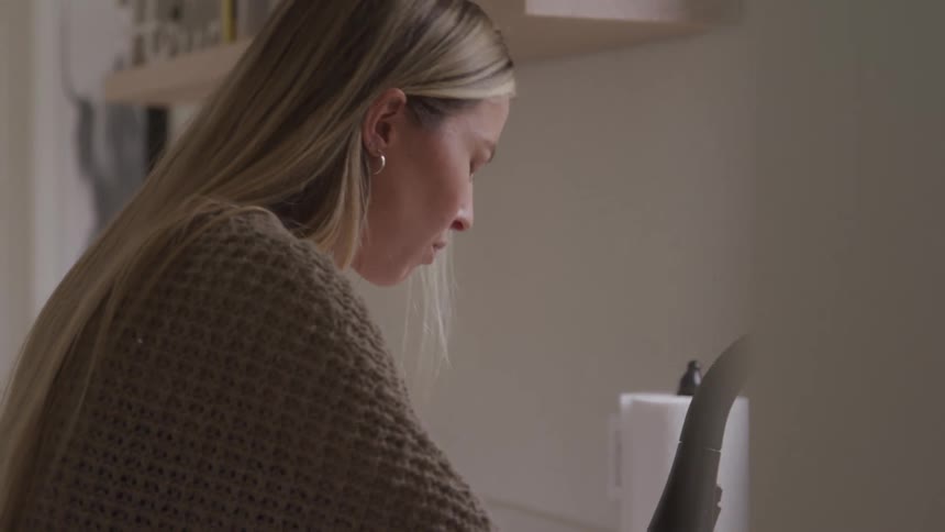 A young woman stands in front of a kitchen sink looking disappointed
