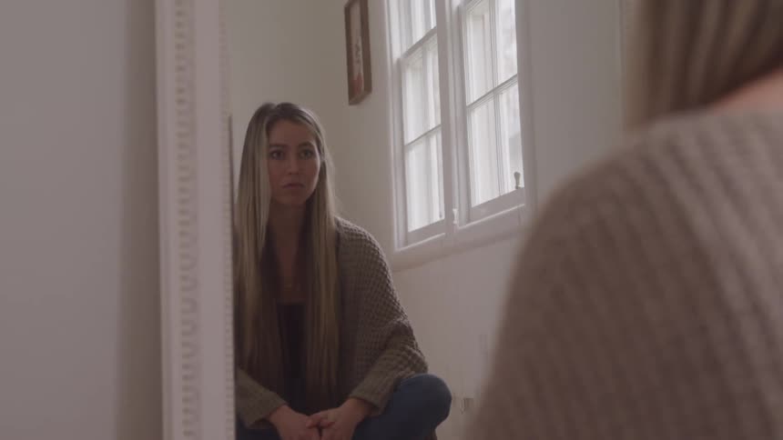 Blonde woman sitting cross legged on the floor faces her reflection in a floor mirror
